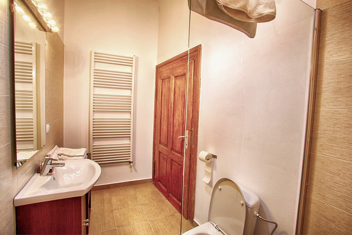 Baia unei camere superioare, cu radiator port-prosop, lavoar și ușă de lemn.