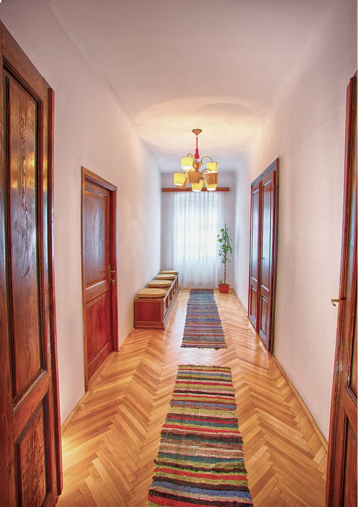 Coridorul casei, cu parchet în spic, uși duble de lemn brun-roșcat și preșuri țesute multicolore pe toată lungimea.