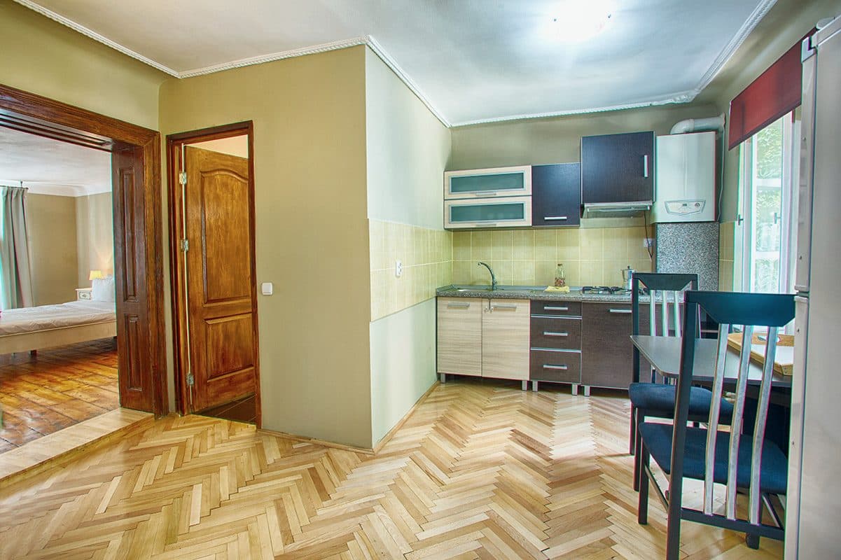 Bucătăria proprie a studioului, cu mobilier albastru închis, chiuvetă, plită și masă cu scaune.
